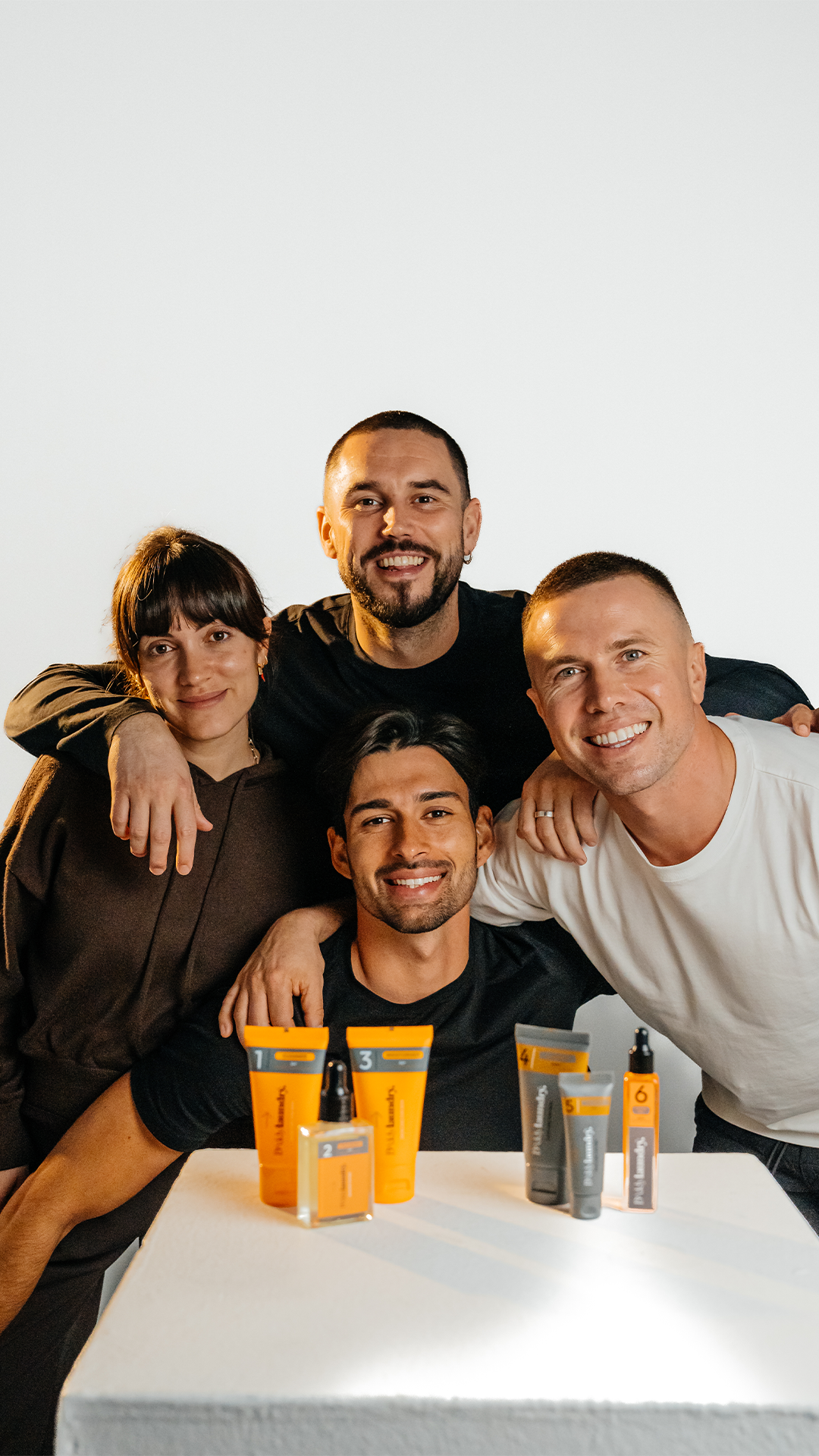 Four people posing with skincare products on a white surface